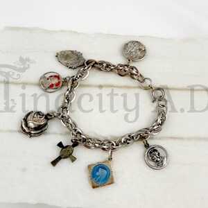 Peut inclure: Un bracelet à breloques en métal argenté composé de plusieurs pendentifs suspendus, dont une rose en trois dimensions, une croix, une icône religieuse carrée en émail bleu et divers médaillons métalliques circulaires et ovales gravés.