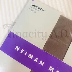 May include: A close-up of a package for sheer Lycra sandalfoot stockings. The package is white with purple trim and the text "SHEER LYCRA® Sandalfoot Stockings" is printed on the front. The text "NEIMAN MARC" is printed in white on a purple background.