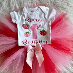 Puede incluir: Un body blanco con el texto "Berry 1st Birthday" en letras rosas y gr&aacute;ficos de fresas. El body se combina con un tut&uacute; de tul rosa y rojo con un lazo de sat&eacute;n rosa.