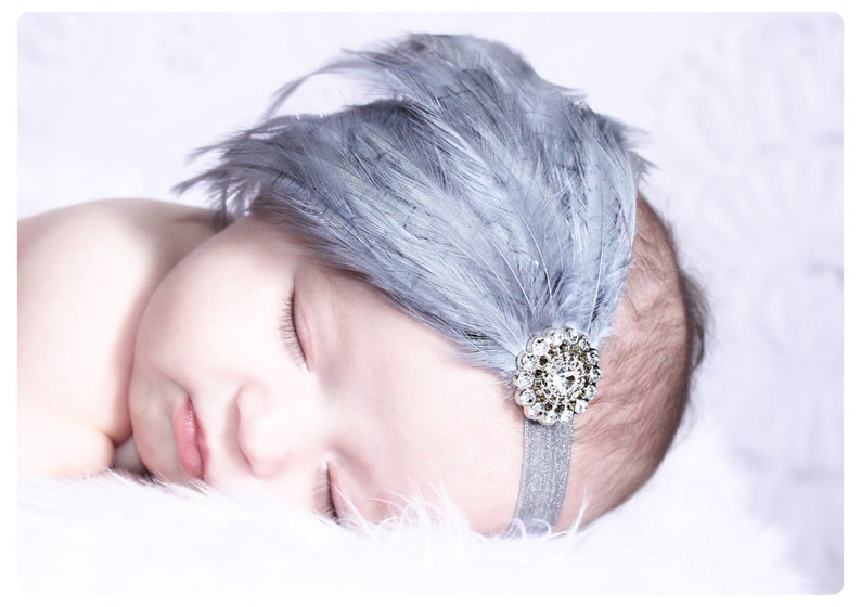 Puede incluir: Un beb&eacute; durmiendo con una diadema de plumas grises con un adorno de pedrer&iacute;a plateada.