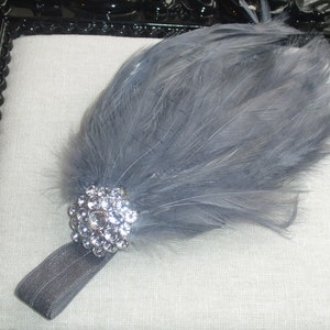 Puede incluir: Una diadema de plumas grises con un gran adorno de pedrer&iacute;a transparente. La diadema est&aacute; hecha de una fina banda el&aacute;stica gris.