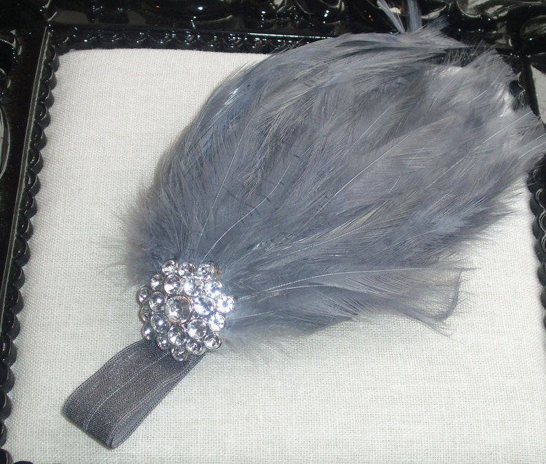Puede incluir: Una diadema de plumas grises con un gran adorno de pedrer&iacute;a transparente. La diadema est&aacute; hecha de una fina banda el&aacute;stica gris.