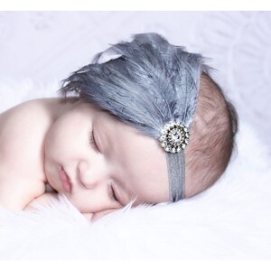 Puede incluir: Un beb&eacute; durmiendo con una diadema de plumas grises con un acento de strass brillante.