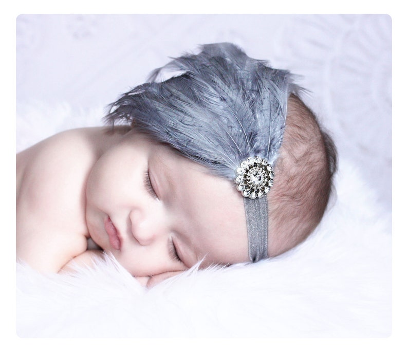 Puede incluir: Un beb&eacute; durmiendo con una diadema de plumas grises con un acento de strass brillante.