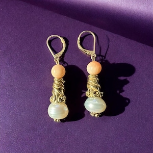May include: A pair of gold earrings with a peach-colored bead and a white pearl bead on each earring.