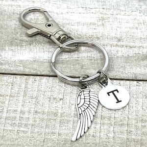 May include: Silver keychain with a silver angel wing charm and a silver charm with the letter T.