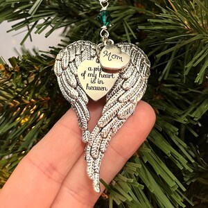 May include: Silver angel wing ornament with a heart that says "a piece of my heart is in heaven" and a smaller heart that says "Mom". The ornament has a green crystal bead.
