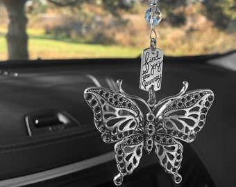 May include: Silver car charm featuring a delicate butterfly design with crystal accents. The charm hangs from a silver chain and includes a silver tag with the inscription "find joy in the journey".