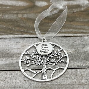 May include: Silver tree of life ornament with a round tag that reads "The love between a mother and her daughter is forever".
