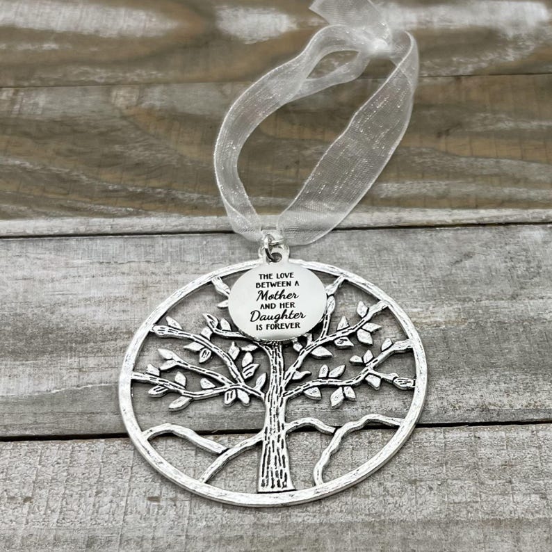 May include: Silver tree of life ornament with a round tag that reads "The love between a mother and her daughter is forever".