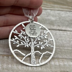May include: Silver tree of life ornament with a round tag that reads "The love between a Mother and her Daughter is forever".
