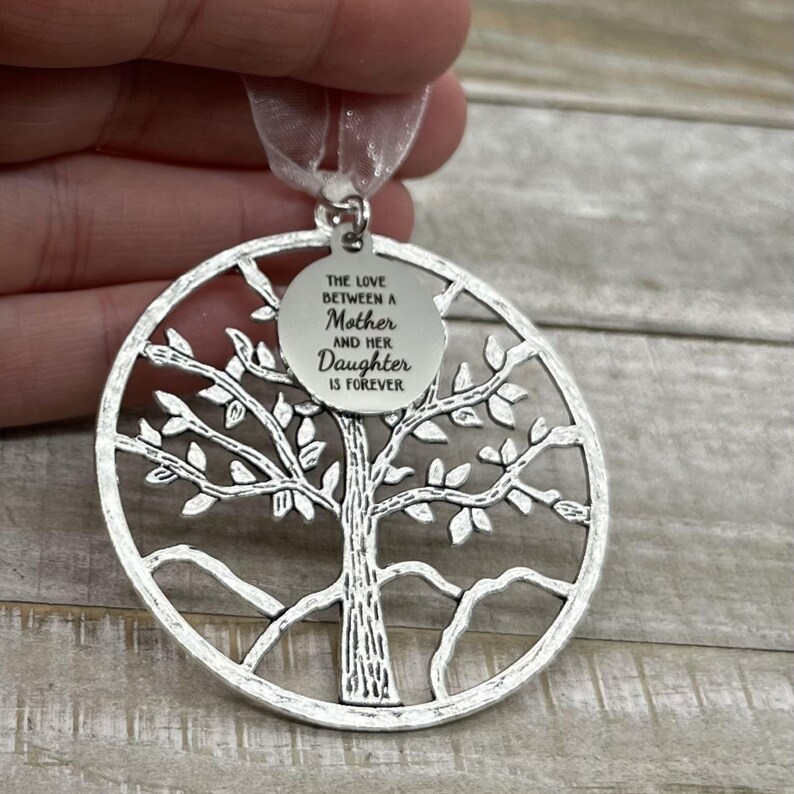 May include: Silver tree of life ornament with a round tag that reads "The love between a Mother and her Daughter is forever".