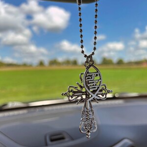 May include: A silver car charm featuring a cross with a fish design. The fish has the word "Faith" inscribed on it.