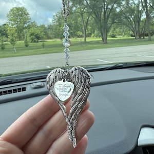 May include: A silver-colored car charm in the shape of angel wings, with a heart-shaped pendant that reads "I have an Angel in Heaven; I call him Grandpa." The charm hangs from a beaded chain.