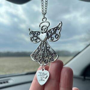 May include: Silver angel car charm with intricate wing and body details. The charm has a heart-shaped center and a smaller heart pendant that reads "I have an Angel in Heaven, I call her Mom."