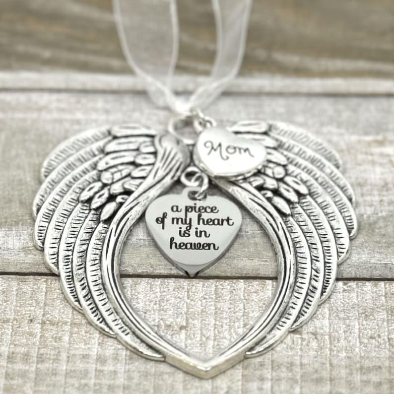 Puede incluir: Adorno de alas de &aacute;ngel de plata con un dije en forma de coraz&oacute;n que dice "a piece of my heart is in heaven" y un dije m&aacute;s peque&ntilde;o que dice "Mom".