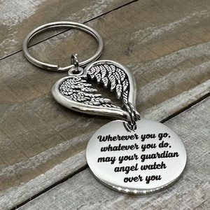 May include: Silver-colored keychain featuring a heart-shaped pendant with angel wings and a round charm. The charm is engraved with the text: "Wherever you go, whatever you do, may your guardian angel watch over you."