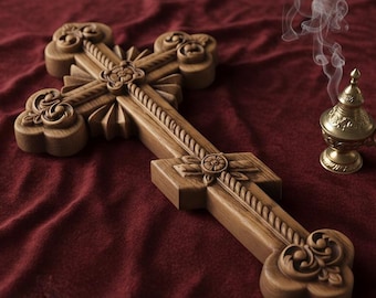 May include: A detailed wooden cross with carved patterns rests on a deep red cloth. A small, gold-coloured incense burner releases smoke, indicating a religious context. The cross showcases elaborate floral and scrollwork designs.