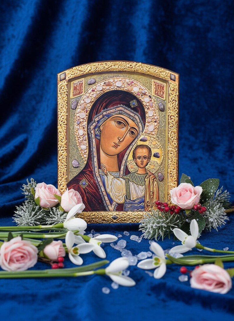 May include: An icon featuring a religious image of a woman and child, framed in gold. The icon is surrounded by pink roses, white flowers, and greenery, set against a deep blue velvet background.