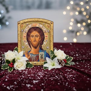 May include: A religious icon featuring a depiction of Jesus Christ, framed in gold. The image is surrounded by white roses, holly, and pinecones, set against a burgundy velvet backdrop with a snowy effect.