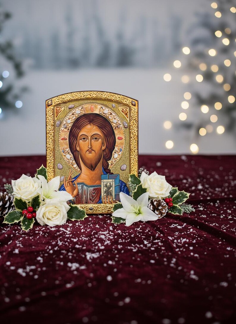 May include: A religious icon featuring a depiction of Jesus Christ, framed in gold. The image is surrounded by white roses, holly, and pinecones, set against a burgundy velvet backdrop with a snowy effect.
