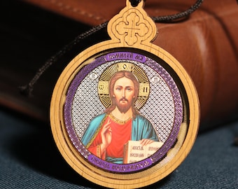 May include: A round wooden pendant with a religious icon of Jesus Christ. The icon is surrounded by a silver-colored border and a purple inscription that reads "ПОМИЛУЙ МЯ". The pendant is attached to a black cord with a wooden bead.