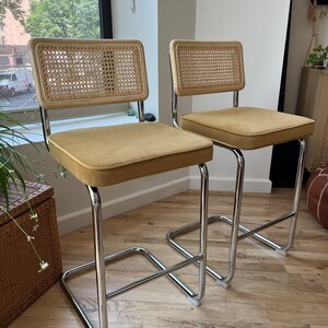 May include: Two chrome bar stools with woven cane backs and mustard yellow velvet seats.