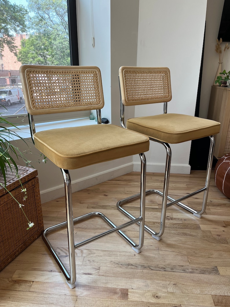 May include: Two chrome bar stools with woven cane backs and mustard yellow velvet seats.