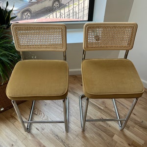 May include: Two mustard yellow velvet upholstered chairs with cane backs and chrome frames.