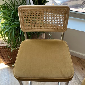 May include: A mustard yellow velvet upholstered chair with a woven cane back and chrome legs.