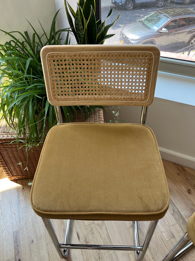 May include: A mustard yellow velvet upholstered chair with a woven cane back and chrome legs.