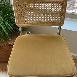 May include: A mustard yellow velvet chair with a woven cane back and chrome legs.