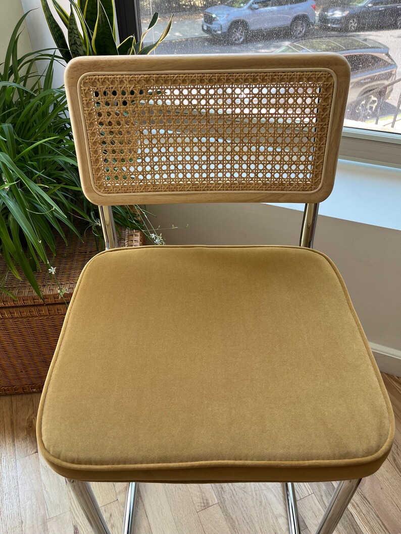 May include: A mustard yellow velvet chair with a woven cane back and chrome legs.