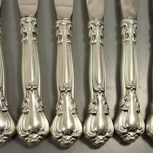 May include: Set of six silver-plated dinner knives with ornate handles. The handles have a detailed floral design and a polished finish.