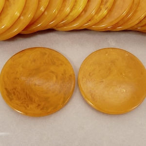 May include: Close-up of several amber-colored, round, flat discs. Two discs are in the foreground, with a swirling pattern. The discs are made of a translucent material. A stack of similar discs is in the background.