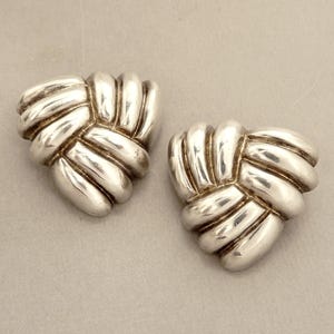 May include: A pair of silver earrings with a knotted design. The earrings are triangular in shape and have a shiny finish.