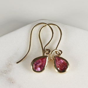 May include: A pair of gold earrings with pink teardrop-shaped gemstones.