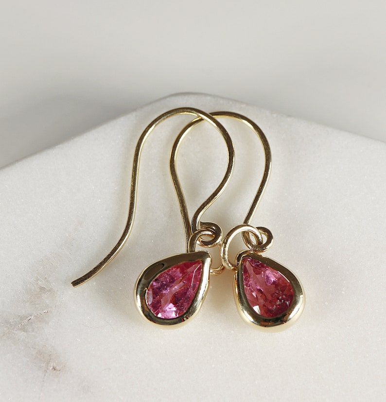 May include: A pair of gold earrings with pink teardrop-shaped gemstones.