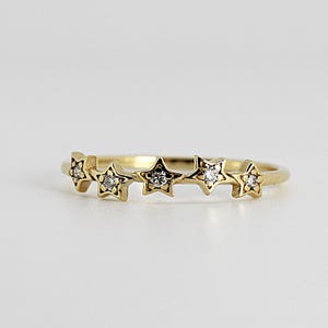 A gold ring with five diamond-studded stars, slightly angled on a white background.