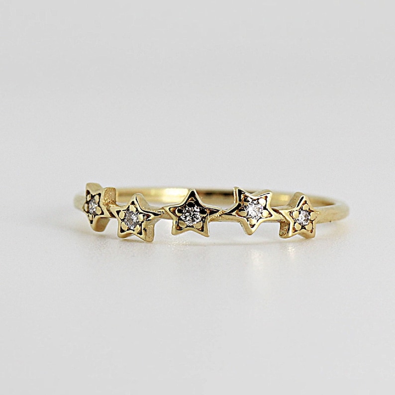 A gold ring with five diamond-studded stars, slightly angled on a white background.