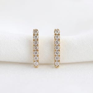 Two vertical gold diamond-pave bar earrings placed upright on a white fabric surface.