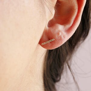 Close-up of a person wearing a single gold diamond bar earring angled along the earlobe.
