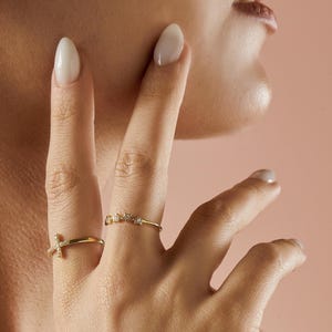 A person's hand with two gold rings: one with a diamond-studded cross and another with five diamond-studded stars.