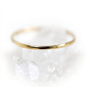 May include: A thin, polished gold ring with a smooth, rounded band. The metal surface reflects light, creating a bright, metallic sheen along the circumference of the circular jewelry piece, which is presented in a clear, focused, and simple manner.