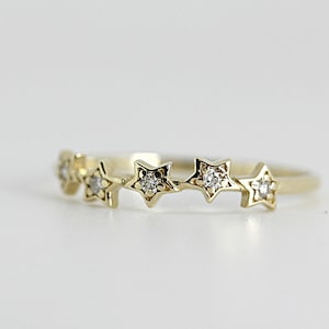 A gold ring with five diamond-studded stars, slightly angled on a white surface.