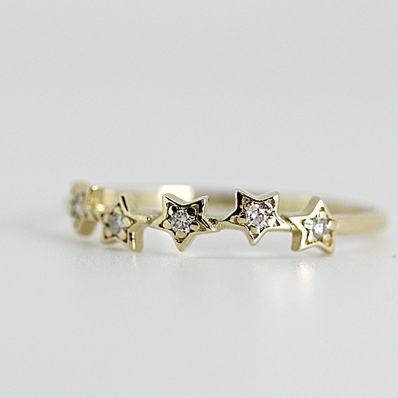 A gold ring with five diamond-studded stars, slightly angled on a white surface.