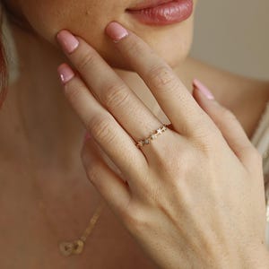 A person's hand wearing a gold ring with five diamond-studded stars, with a blurred gold necklace in the background.