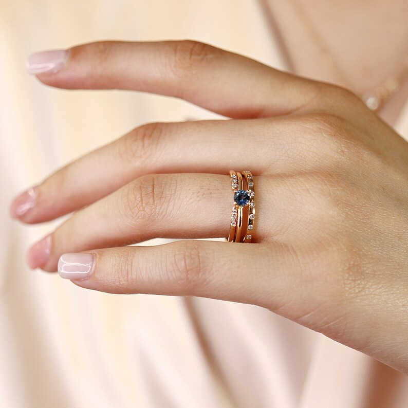 Puede incluir: Un anillo de oro con una piedra preciosa de zafiro azul y diamantes m&aacute;s peque&ntilde;os engastados en una banda delicada.
