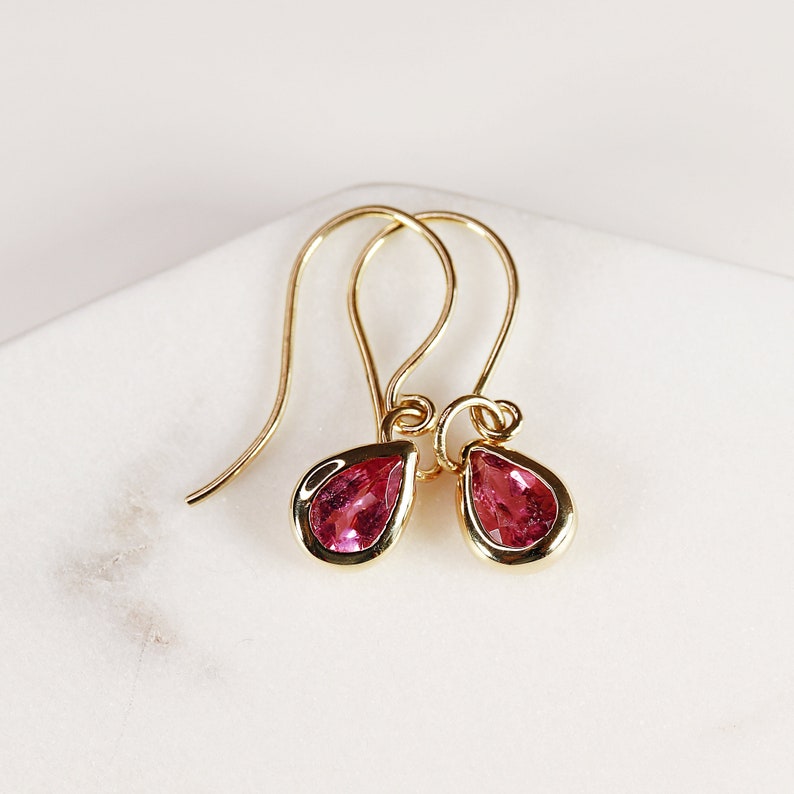 May include: A pair of gold earrings with pink teardrop-shaped gemstones.