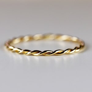 May include: A thin gold band ring with a braided design.